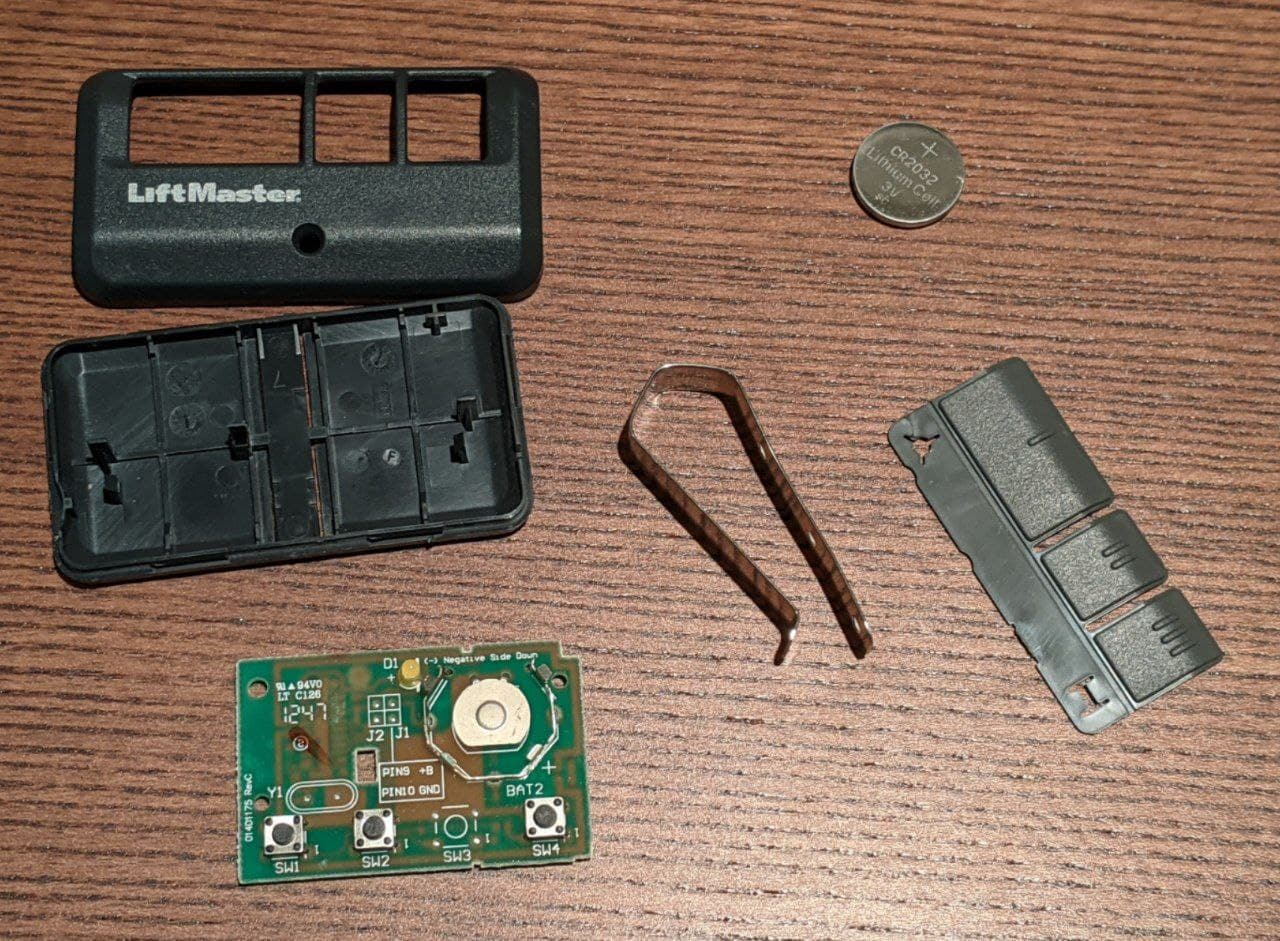 the six parts of the spare remote on my desk: metal clip, plastic buttons, battery, PCB, and two halves of the case